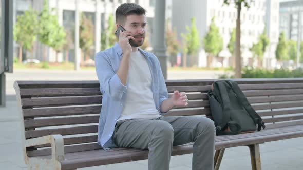 Angry Young Man Talking on Phone While Sitting on Bench