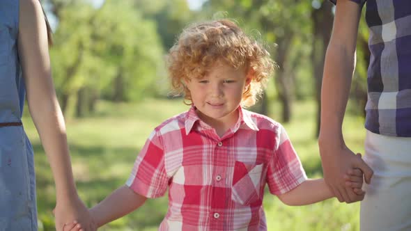 Portrait of Happy Redhead Little Boy Taking Hands of Unrecognizable Brother and Sister Walking Away