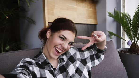 Happy Brunette Girl Dressed in Plaid Shirt Smiling Posing Makes Peace Signs with Fingers Making Self