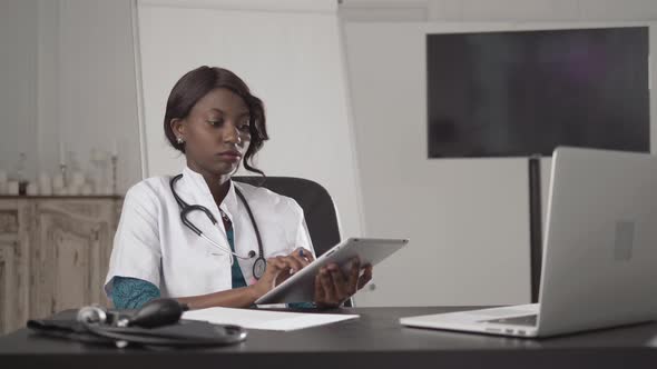 Attractive African Medical Doctor Talking on Telephone Work with Laptop, in Cabinet Hospital, Write