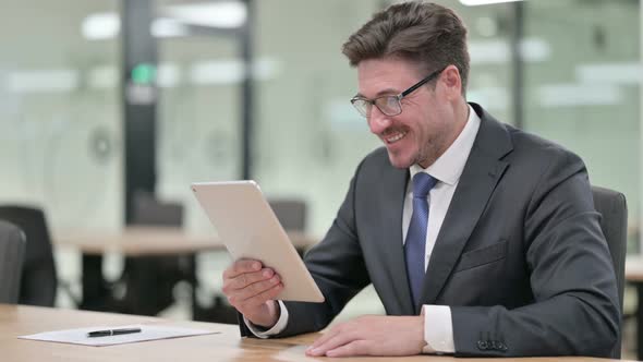 Professional Middle Aged Businessman Doing Video Chat on Tablet in Office