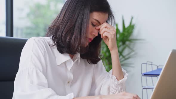 Asian young business woman working on computer and feeling headache from too much workload in office