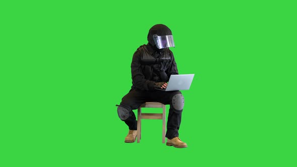 Riot Police Officer Sitting and Using Laptop on a Green Screen Chroma Key