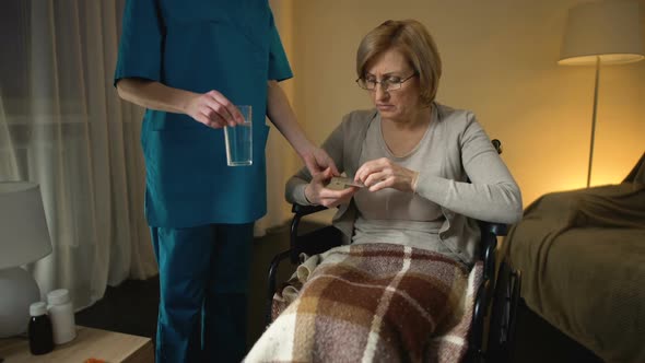 Female Carer Giving Pills to Hospital Patient in Wheelchair, Rehabilitation