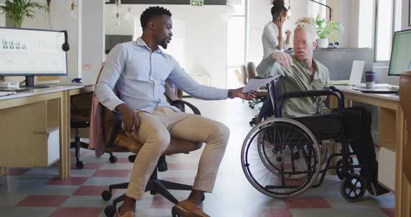 Diverse business people discussing with disabled colleague and documents in creative office