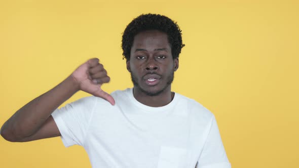 African Man Gesturing Thumbs Down, Yellow Background