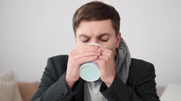 Sick Young Man Sitting on the Sofa Wrapped in Blanket