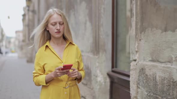 Crop View of Natural Blond Woman Looking at Phone Screen While Walking at Old City Street. Young