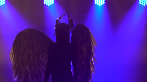 Silhouette of Dancing Greek Goddess Artemis with Wings on Stage in a Dark Studio with Smoke and Neon