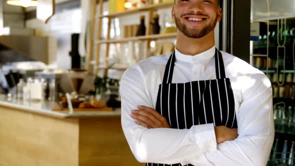 Portrait of smiling waiter standing with arms crossed