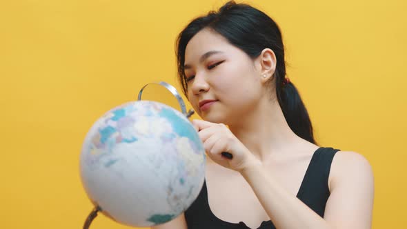 Young Asian Woman Examining the Globe with a Magnifying Glass