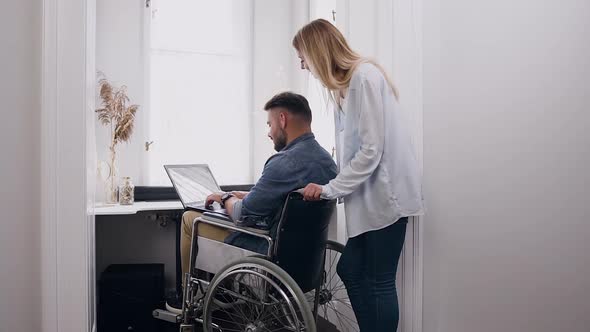 Man in Wheelchair Working on Laptop at Home and Secretly Looking at His Wife