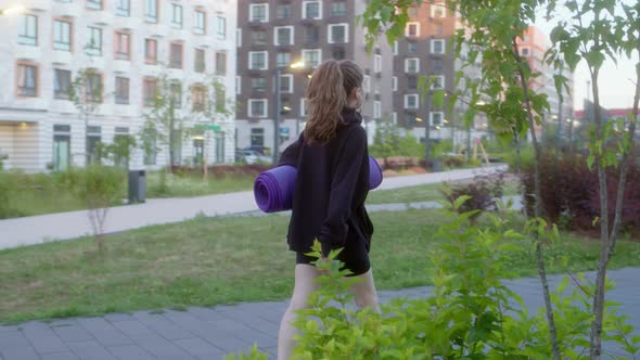 Handheld Athletic Fit Woman Walks Down Street in Her Residential Complex in Black Sweater and with