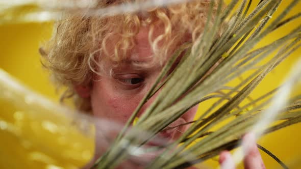 Closeup Green Floral Stems with Small Yellow Flowers and Face of LGBT Man with Nose Piercing Looking