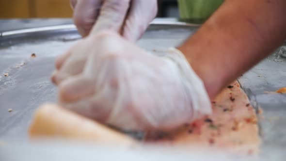 Spatula slowly gathers up Thai rolled ice cream from cold plate, slow motion close up 4K