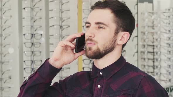 Cheerful Young Man Talking on the Phone at the Optician Store