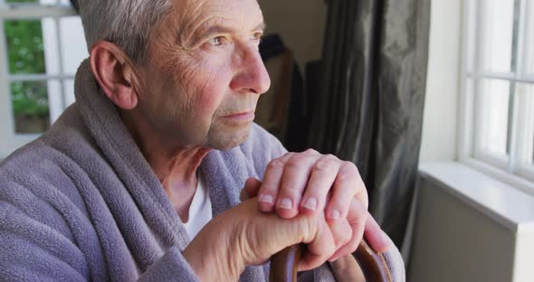 Sad senior caucasian man wearing bathrobe sitting by window