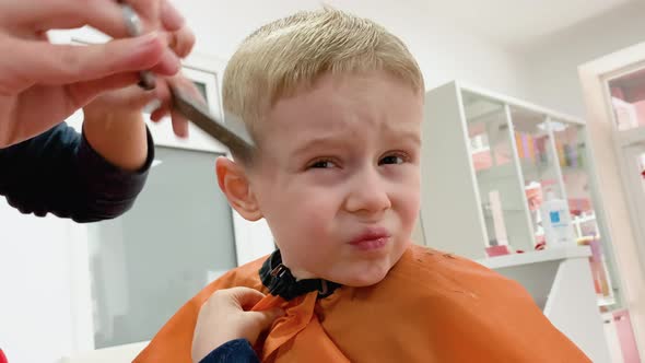 Cute Blond Smiling Baby Boy in a Barber Shop Having Haircut By Hairdresser
