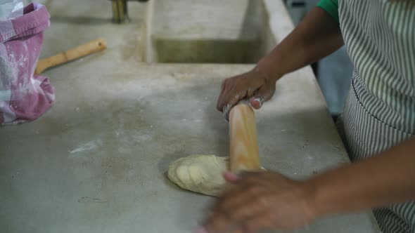 Mature Latin woman kneading flour dough with rolling pin in old vintage kitchen