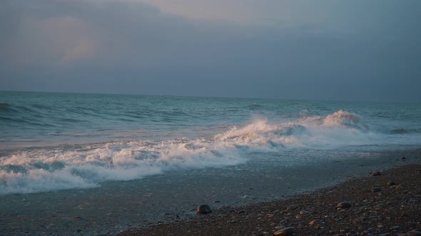 Beach Shore with Pebbles Sand on the Sunset with Strong Waves Crushing