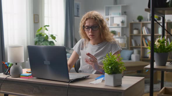 Young Woman at the Desk in the Living Room Counts the Costs in Checks