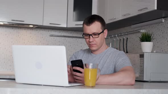 A Man During Remote Work From Home Writes Data From a Phone To a Laptop While Sitting at a Table