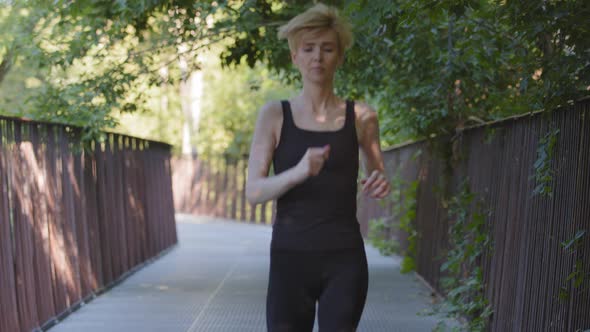Middleaged Athletic Slim Woman Trainer Caucasian Lady Wears Black Tracksuit Runs on Bridge in Park