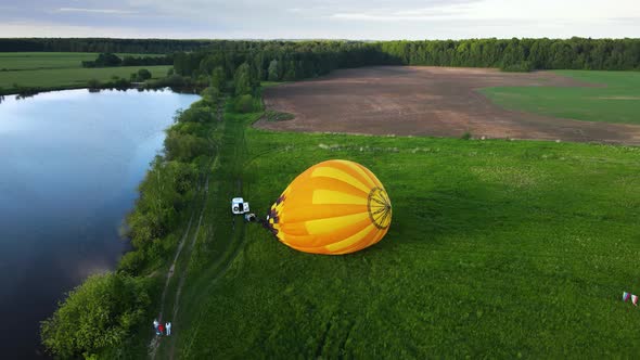 Family oversees preparation of large yellow air balloon for flight on river bank
