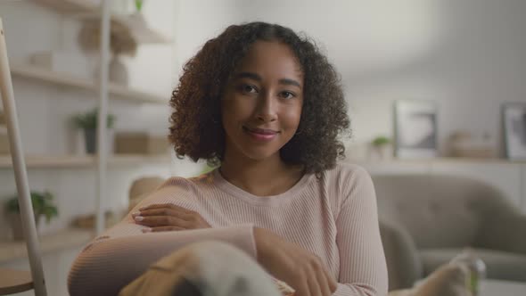 Young Cute African American Curly Woman Resting on Sofa Smiling to Camera at Living Room Interior