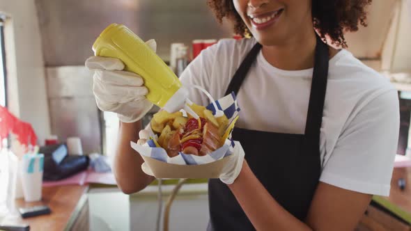 African american woman wearing apron putting mustard over the hot dog in food truck