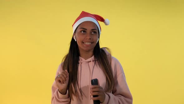 Happy African Woman in Santa Hat and Wireless Headphones Listening to the Music