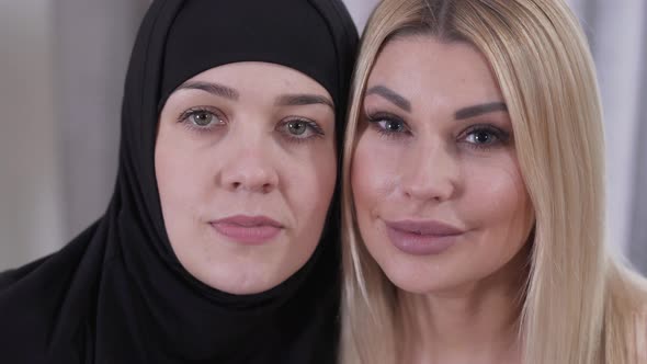 Close-up Faces of Muslim Woman in Hijab and Caucasian Blond Lady. Two Different Women From Different