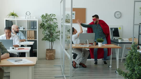 Funny Young Man in Super Hero Costume Running in Office Doing Highfive with Colleagues