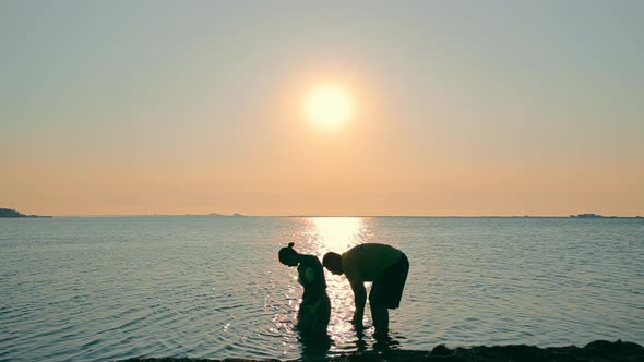 Silhouette of a Man Washing a Young Girl in the Sea at Sunrise