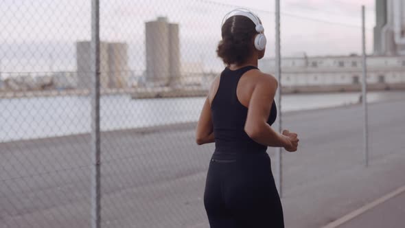 Young Woman In Black Sportswear Jogging Along Harbour