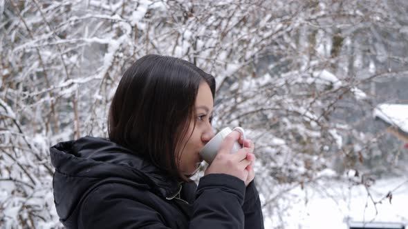 Young asian female drinking cup of tea in winter scenery in slow motion