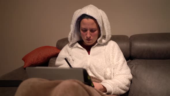 young woman dressed in bunny pajamas uses tablet and writes
