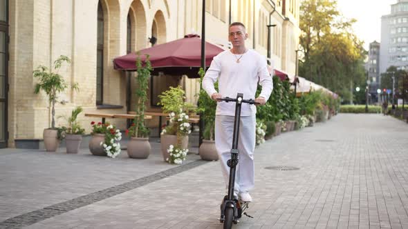 Wide Shot Millennial Man Riding Electric Scooter on City Street in Slow Motion