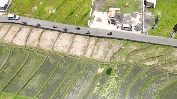 aerial drone shot of countryside highway of electric scooter convoy alongside empty rice fields on a