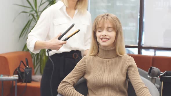 Beautiful Caucasian Client Sitting in Hair Salon While Hairdresser Is Combing Her Long Hair