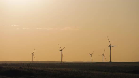 Silhouette Windmills for Electric Power Production in the Meadow at Sunset. Group of Windmills for