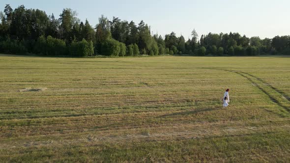 Mom in White Dresses with Her Daughter Walking on a Mown Field in the Summer