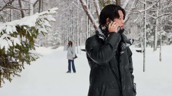 Young Asian Man Talks on His Phone in Winter Forest and Finds His Girlfriend Behind Him