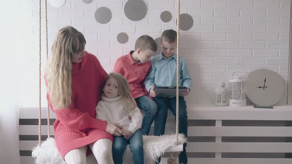 Mom and Daughter Ride on Swing Near Sons Playing on Tablet