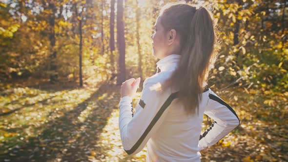 Young Hardy Woman in Sport Clothes is Running By an Autumn Wood on Sunny Day