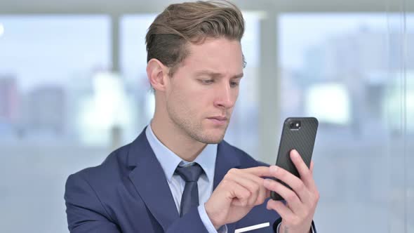 Portrait of Cheerful Young Businessman Using Smartphone in Office