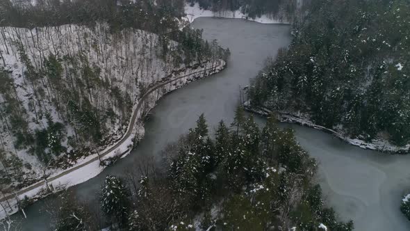 Revealing shot of frozen lake surrounded with forest and fairy tale castle in the distance at winter