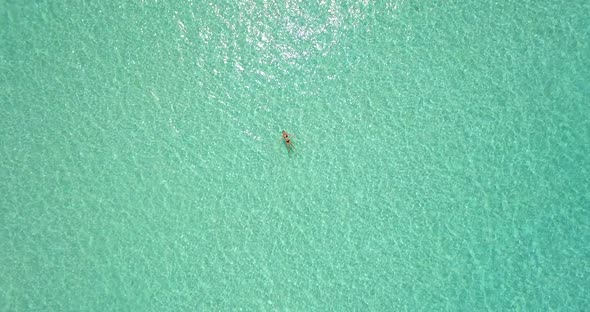 Aerial drone view of a woman floating and swimming on a tropical island