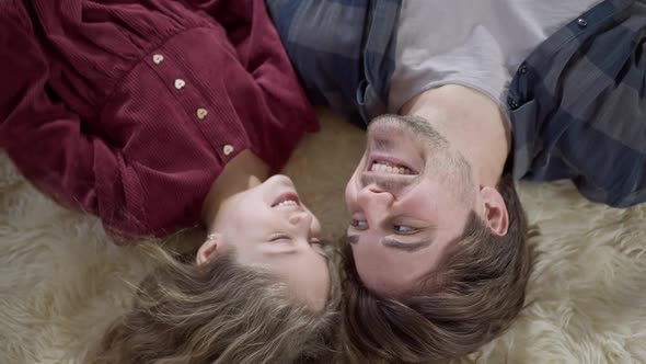 Top View of Happy Caucasian Young Father and Little Daughter Talking Lying on Soft Carpet Looking at