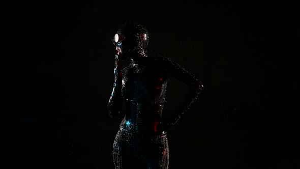 a Woman in a Black Latex Suit Helmet and Glasses Dances on a Dark Background and Licks Palm